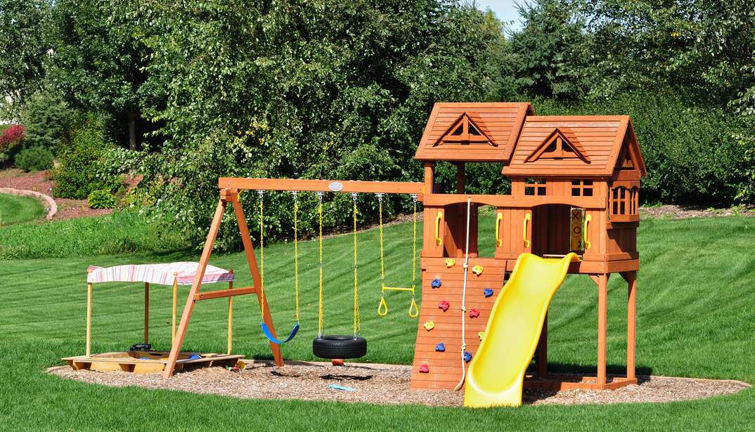 A back yard wooden swing set placed in a garden