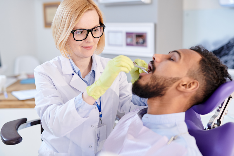 Portrait of smiling female dentist examining teeth of young patient sitting in dental chair