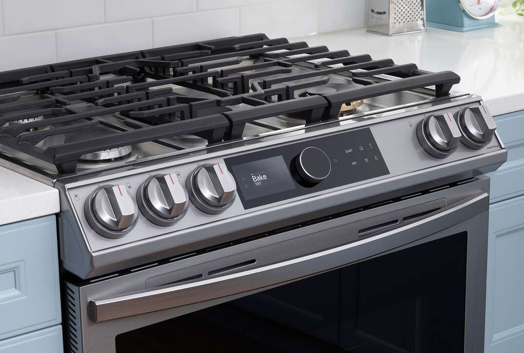 Samsung smart range with black grates on stovetop, a stainless steel frame, black oven door, multiple knobs and a black smart control panel