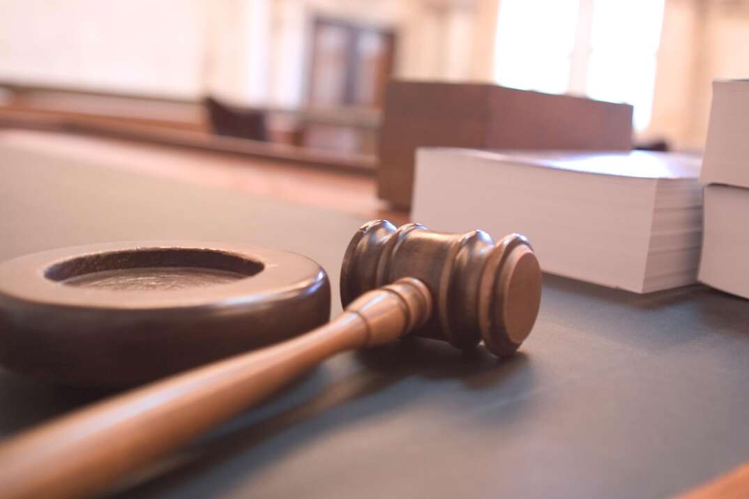 The gavel of a judge sits on a wooden surface ostensibly in a courtroom with thick books sitting on the same table in the background, gavel, judge's gavel, hammer, courtroom, court, legal, legal case, legal matter, law, law books, legal books, thick books, books, wooden table, wooden, wood