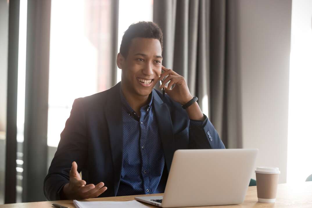 Smiling african american businessman, lawyer, real estate agent, banker or consultant making cell phone call to client at office. Black happy male employee listening to good news using cellphone