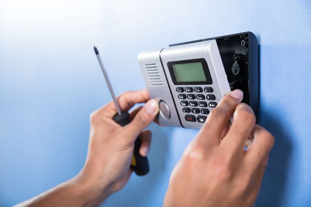 Human Hand Installing Security System On Blue Wall