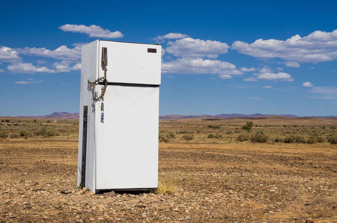 A white colored refrigerator in significant disrepair sits abandoned in an expanse of desolate land against a blue sky with scattered white clouds, refrigerator, fridge, abandoned refrigerator, abandoned fridge, disrepair, old fridge, old refrigerator, obsolete, abandoned, old, desert, prairie, pasture, dead grass, desolation, desolate, white fridge, white refrigerator, blue sky with white clouds, blue sky, sky, white clouds, clouds