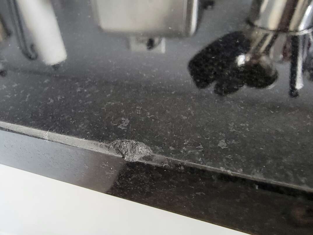Closeup photo of a chip in a black granite countetop.