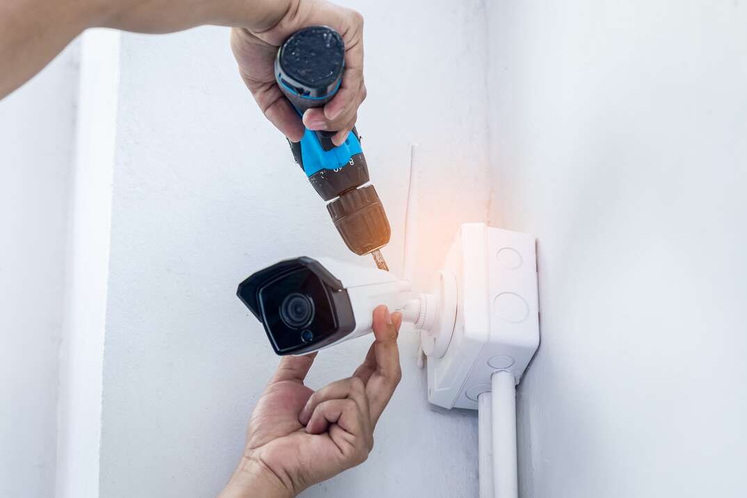 person installing security camera with hand drill