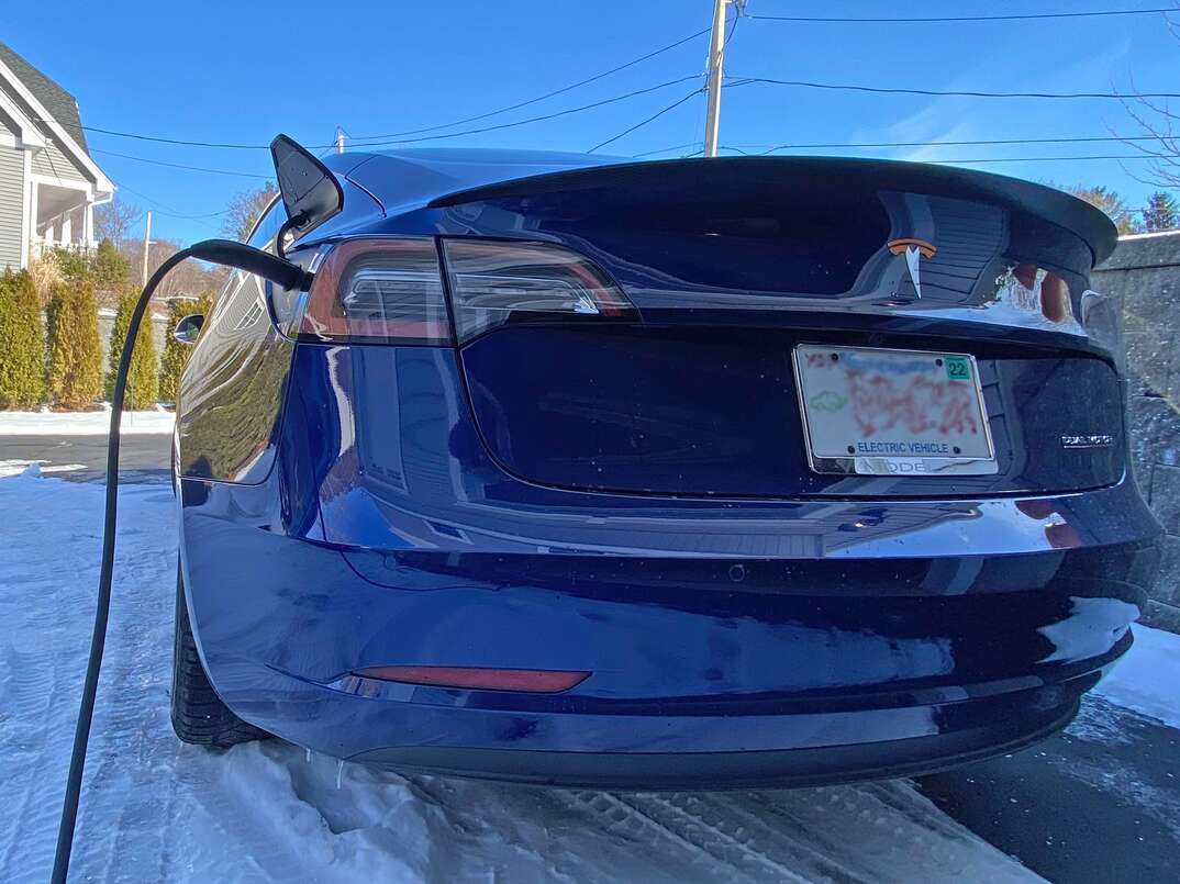 Blue 2018 Tesla Model 3 in a residential driveway getting charged 