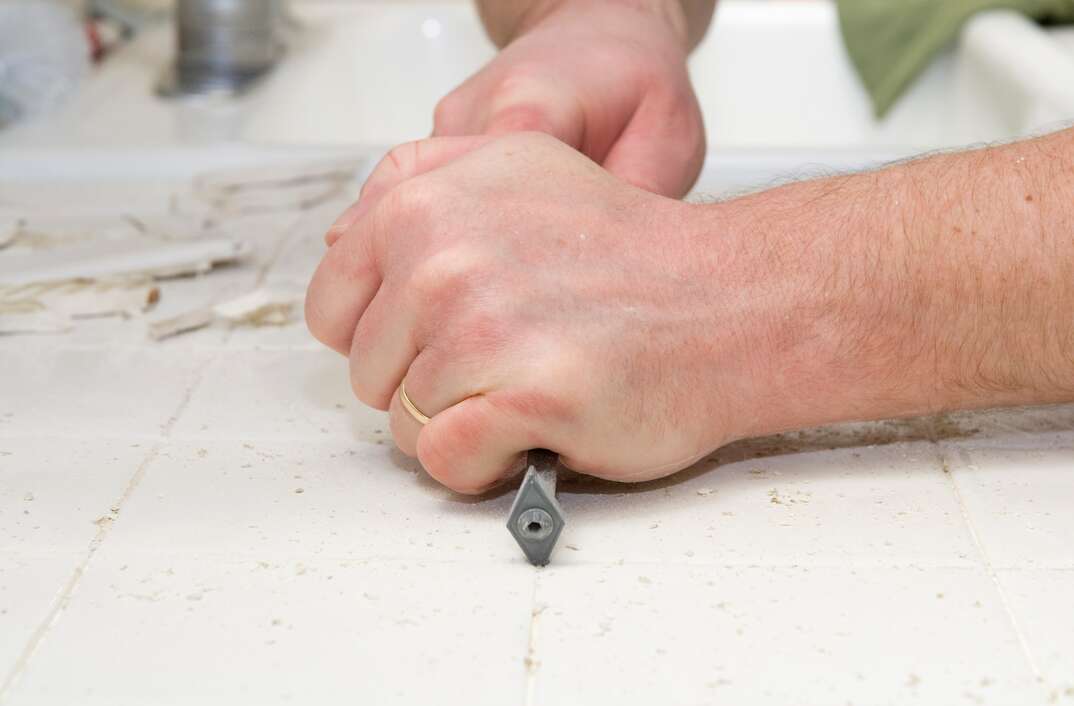 Male hand using a grout removal tool to removing grout from kitchen tiles