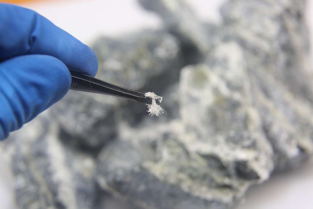 a gloved hand using tweezers to hold Chrysotile asbestos fiber close up.