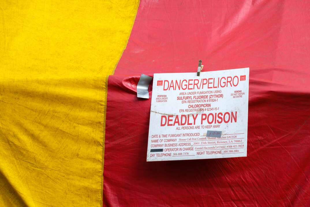 A closeup of a white and red warning sign affixed to the side of a yellow and red striped fumigation tent tells the viewer of deadly poison in English and Spanish, red and yellow striped fumigation tent, fumigation tent, fumigation, tent, warning sign, warning, sign, danger, deadly poison, deadly, poison, English, Spanish