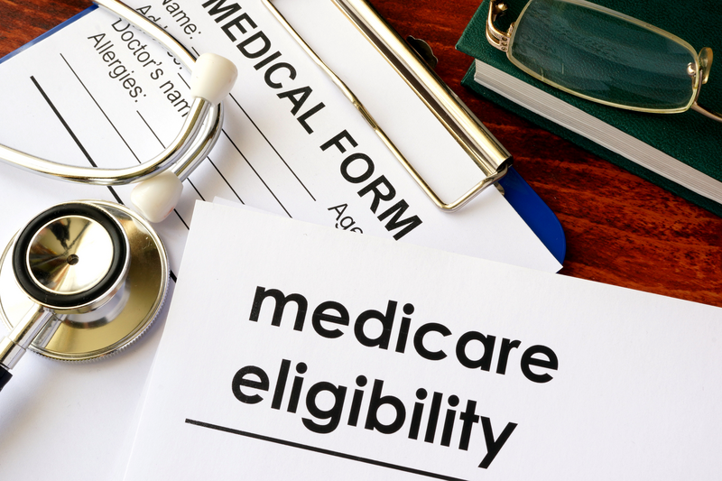 A Medicare eligibility form and other medical documents sit on a woodgrain desk along with a stethoscope, Medicare, Medicare forms, Medicare eligibility, desk, woodgrain, woodgrain desk, stethoscope, forms, documents, health insurance, insurance, health, health coverage, medical coverage