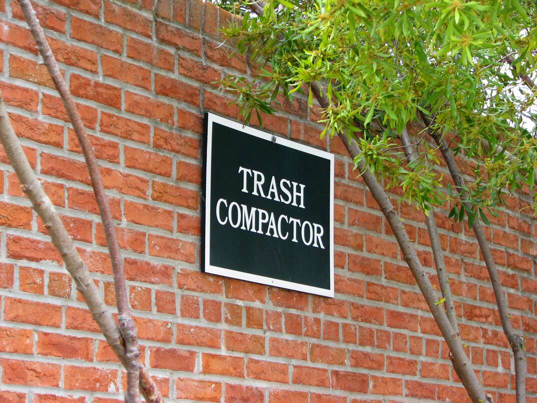 A red brick exterior of a building showing a sign that reads 'trash compactor.'