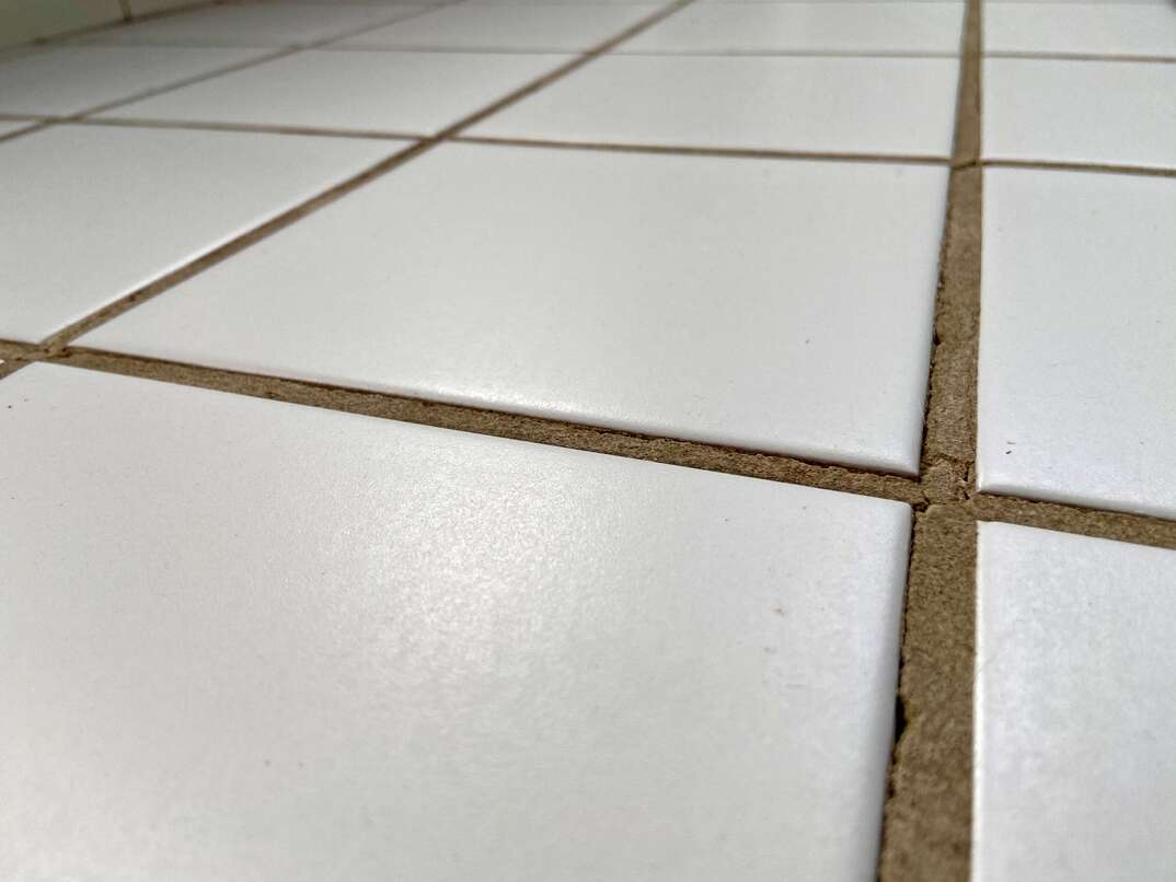close up shot of white square tiles with broken grout