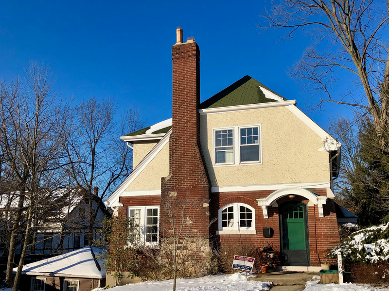A large two story house with a brick chimney sits in the foreground against a backdrop of trees and clear blue skies, blue skies, blue sky, sky, trees, tree, chimney, brick chimney, two-story house, two-story, house, large house, two-story home, home