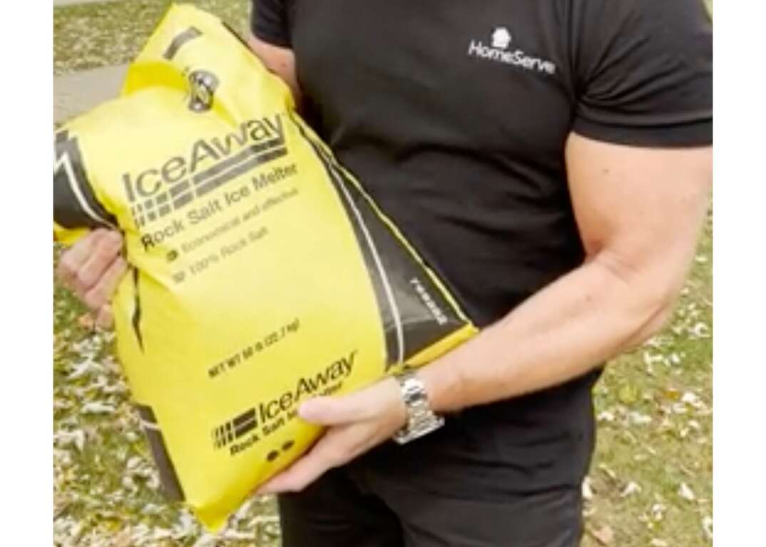 A man prepares to spread Ice Away brand rock salt from a yellow 50 pound bag