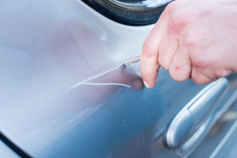 A human hand uses a key to scratch the paint of the exterior of a vehicle in an act of vandalism, vandalism, vandal, criminal damage, criminal, damage, paint job, hand, human hand, key, keying a car, scratch paint, paint, car, vehicle, crime