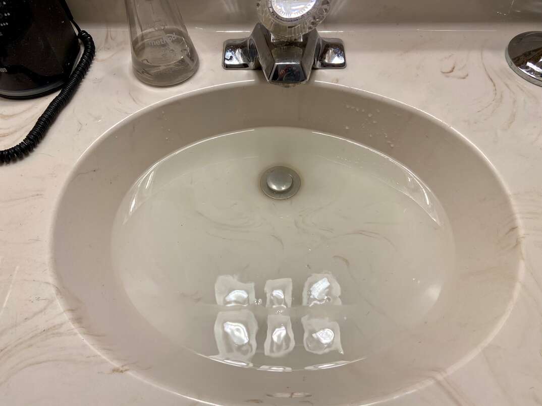 photo is looking down on a residential bathroom sink that is clogged and slowing draining water