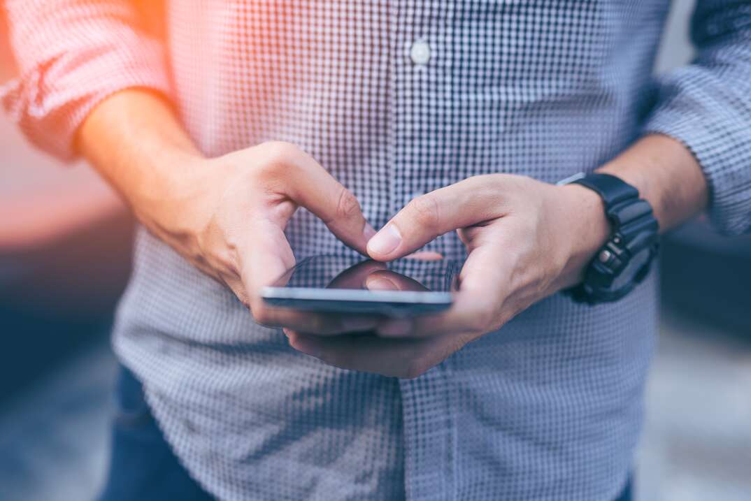 close up of a male torso texting on a phone with a blue dress shirt on