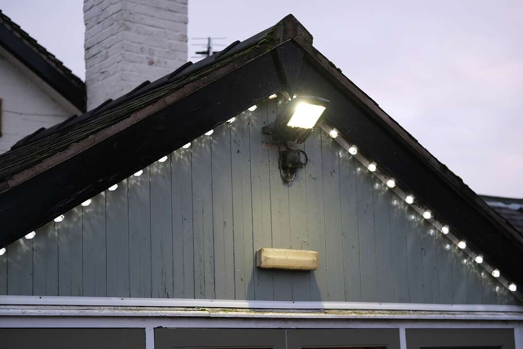 Roof top of the house with installed illumination showing the large flood light and small decorative lights, flood light, light, lights, lighting, outdoor lighting, outdoor, outdoors, motion lights, motion activated lights, motion activated, security, security lights, safety, home security, roof, rooftop, house, home, pointed roof, night light, night, evening, dusk, dark, getting dark, sky, night sky, evening sky, house lights