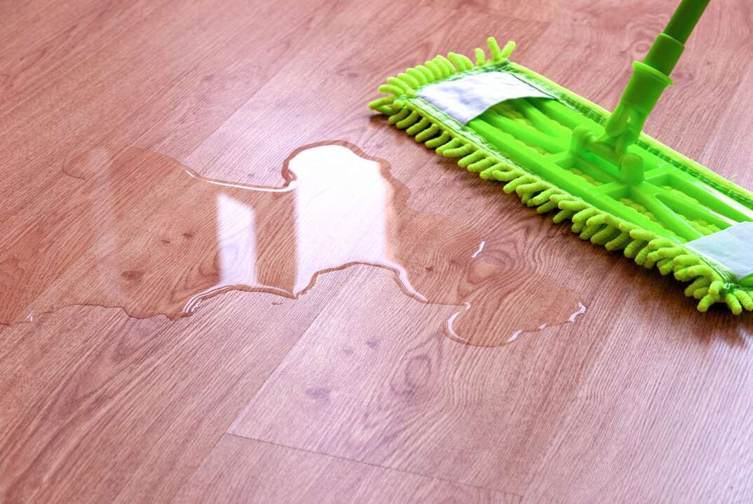 A green mop is used to mop up water from a brown colored hardwood floor