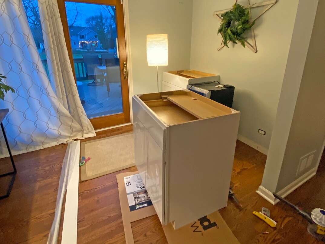 all of the parts needed for the dry bar sit out on the hardwood floor as the shaker cabinets are dry-fit into their new location 