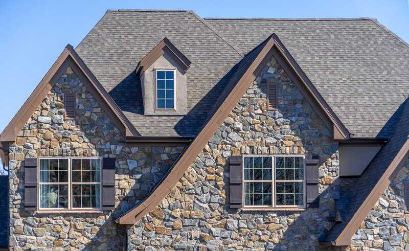 A large house with brown colored stone veneer is shown against a blue sky in the background, large house, brown colored stone veneer, stone veneer, veneer, stone