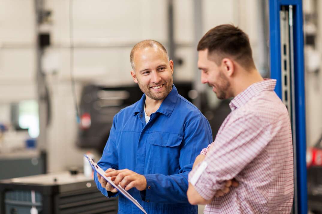 auto service, repair, maintenance and people concept - mechanic with clipboard talking to man or owner at car shop