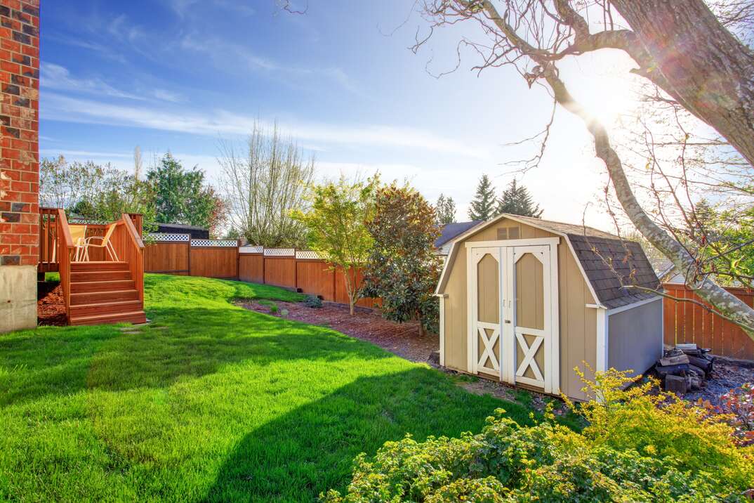 a very color saturated backyard with a tall fence and a barn-style backyard shed in the corner of the lot