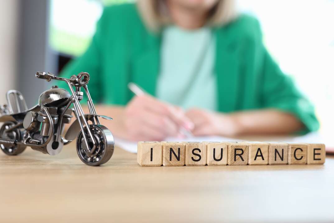 Motorcycle, travel and medical insurance concept. Motorcycle model and word insurance on table, blurred manager with documents in background.