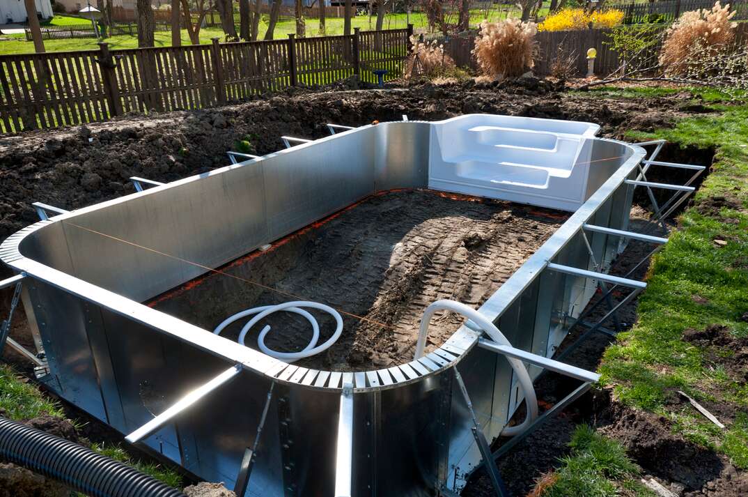 A semi-inground pool getting installed in a backyard. The pool looks like a typical above ground pool but it is set into a hole.