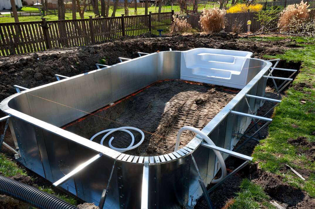 Aluminum sides and support beams are laid out in an excavation during a suburban home swimming pool installation project.