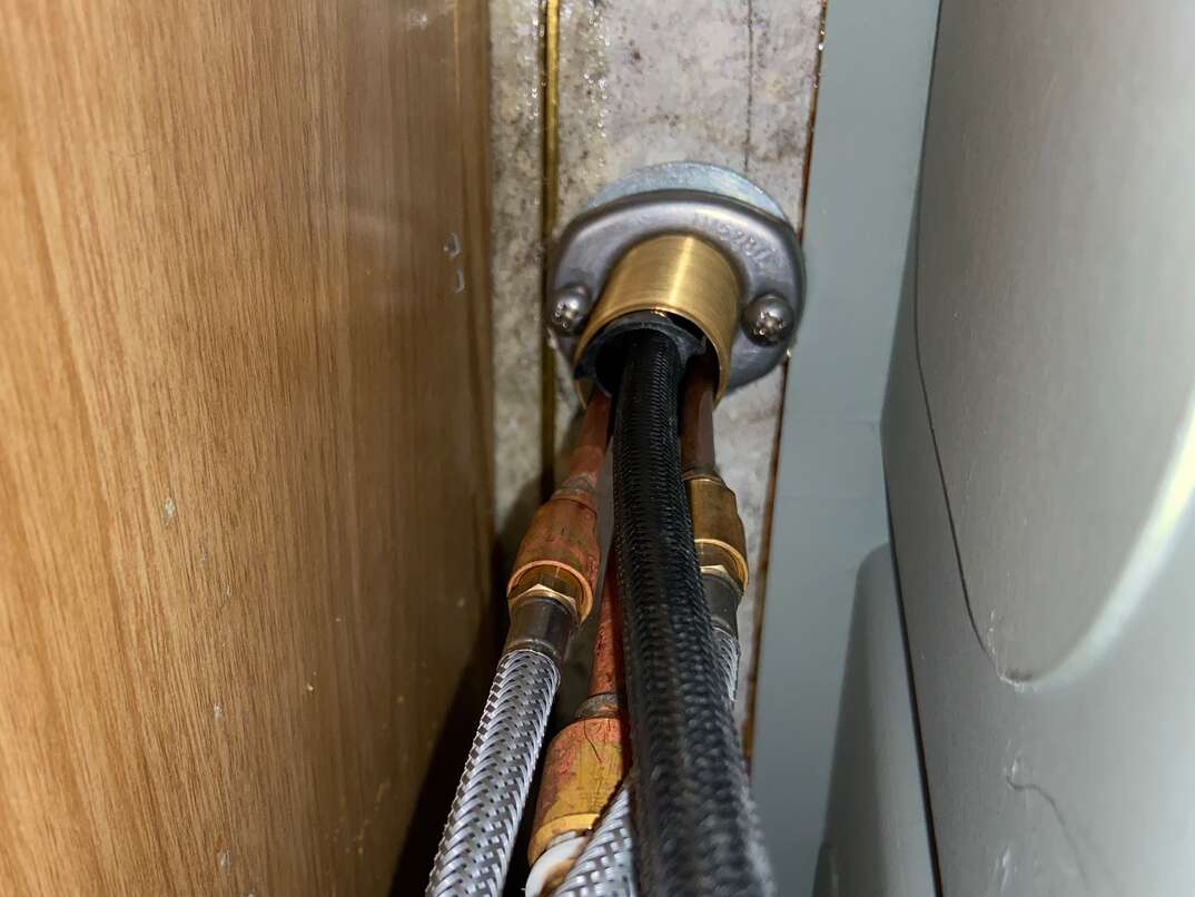 Photo taken underneath kitchen cabinet looking up at the bottom of the faucet 