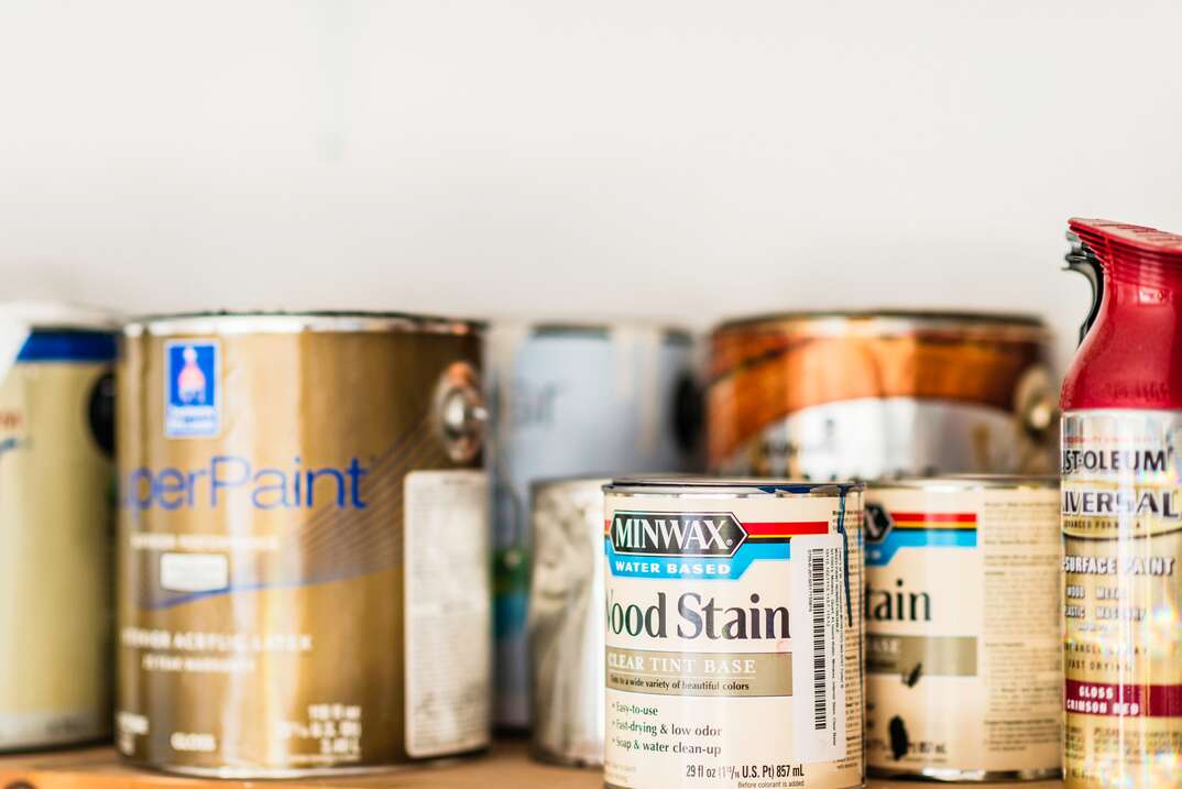 Suffolk, Virginia, USA - June 15, 2014: A horizontal shot of a collection of opened and unopened American brand cans of paint, wood stain and paint sprays organized neatly on a wooden shelf. The brands include cans of indoor house paint by Sherwin Williams, spray paint by Rustoleum, and wood stain by Minwax.