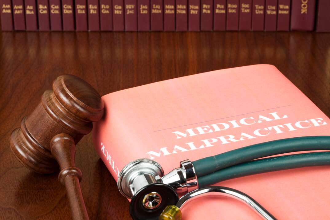 A medical malpractice legal text book sits on a brown wooden table in a legal library with a judge gavel next it and a doctor stethoscope sitting on top of it, medical malpractice, medical, malpractice, stethoscope, gavel, doctor's stethoscope, judge's gavel, legal library, library, legal books, legal text books, legal, law, medical malpractice book, medical malpractice, book, legal text book, text book