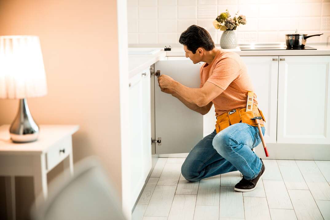 Side view of adult male holding screwdriver and repairing nightstand at home stock photo