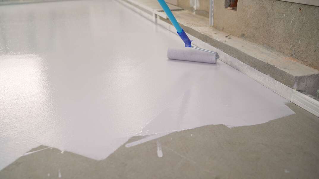 Manual painting of a white floor with a paint roller for waterproofing. A worker paints the concrete floor with white paint. A worker paints the floor with a roller.
