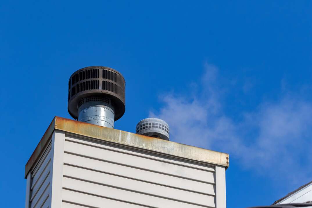 Looking up at white steam or smoke venting out of chimney flue vent pipe for furnace and water heater on a cold winter day. Pollution and energy saving concept