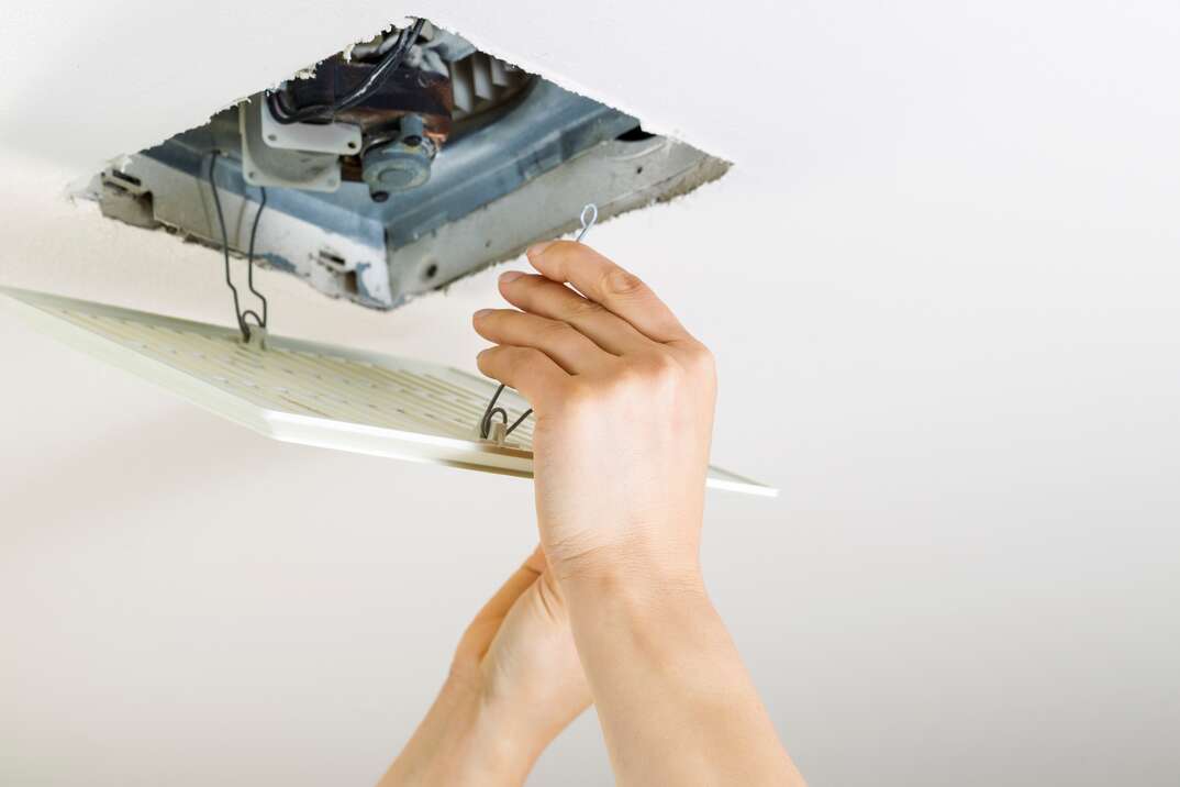 Close up of female hands installing clean bathroom fan vent cover from ceiling