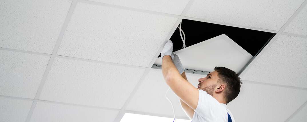 Electrician On Stepladder Installs Lighting To The Ceiling