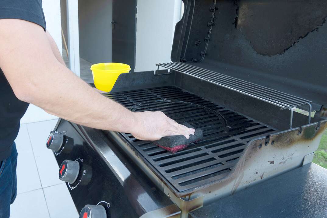 a male s hand cleans a black BBQ grill with a soft brush 