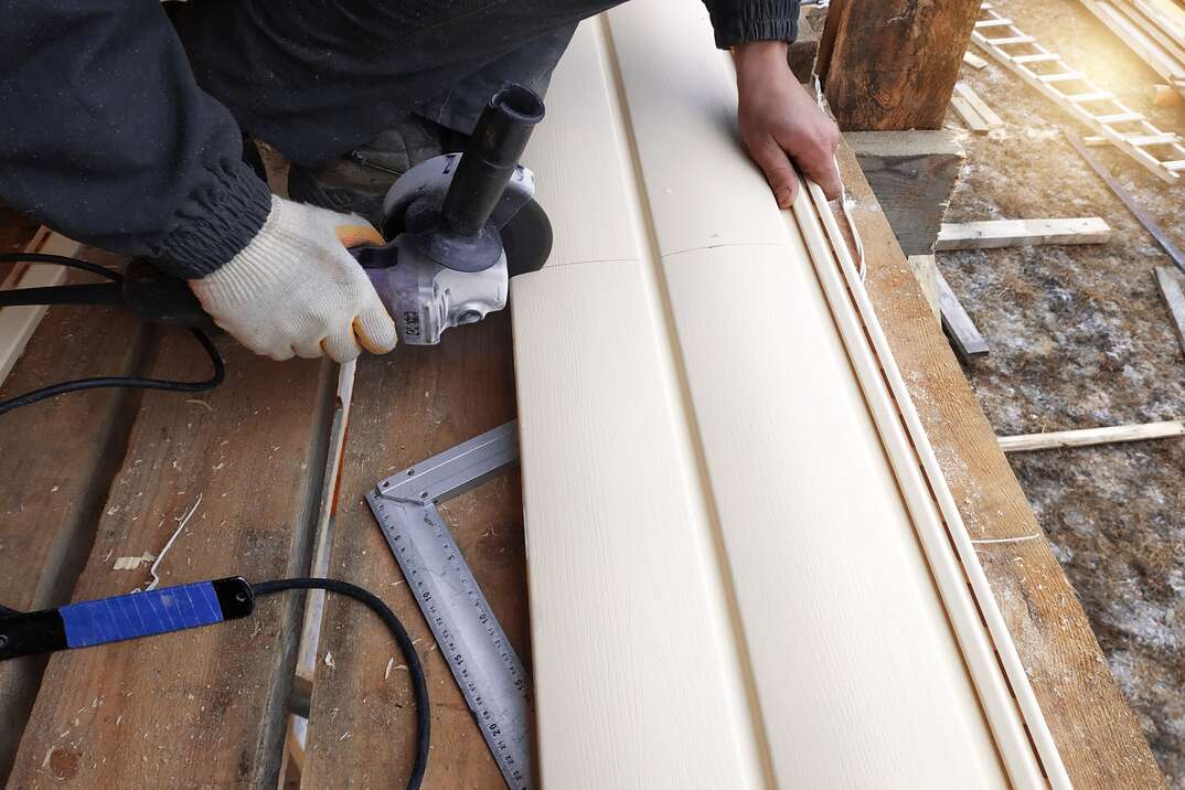 A contractor cuts vinyl siding using a power grinder 