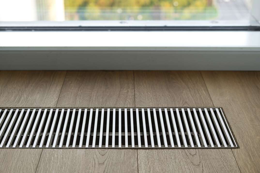 Close up of wooden floor with chrome ventilation grid of central heating against window
