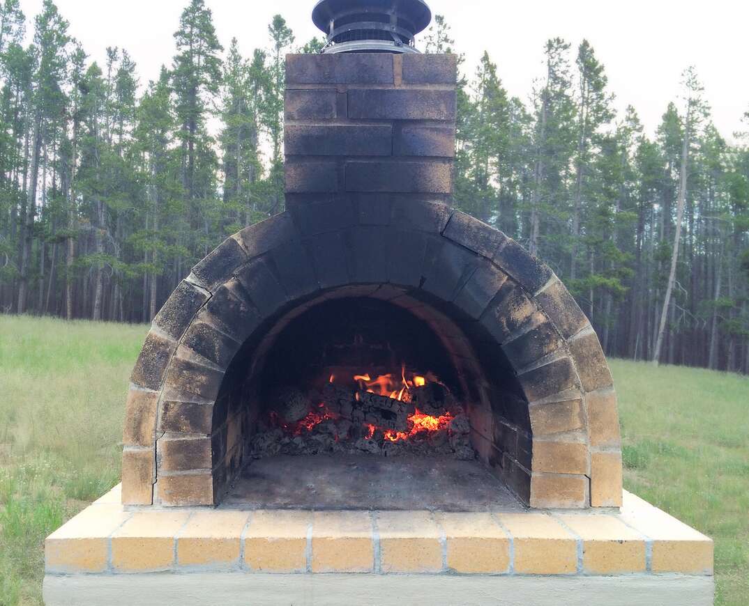 Outdoor Brick Oven In A Grass Clearing Of A Tree Lined Forest