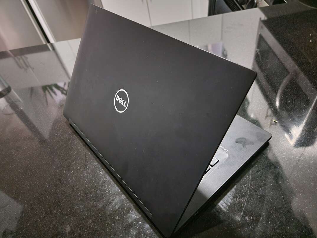 A black colored Dell brand laptop computer sits on a shiny black granite countertop