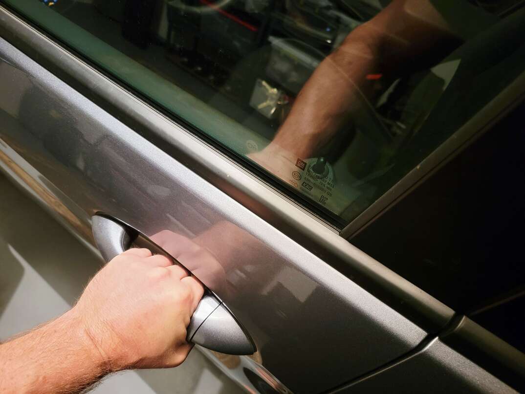 The hand of a man pulls on a vehicle door handle after apparently locking himself out as the keys can be seen inside the car through the window, car window, car door, door handle, car door handle, handle, hand, human hand, male human hand, man's hand, door, window, keys, locked out, lockout