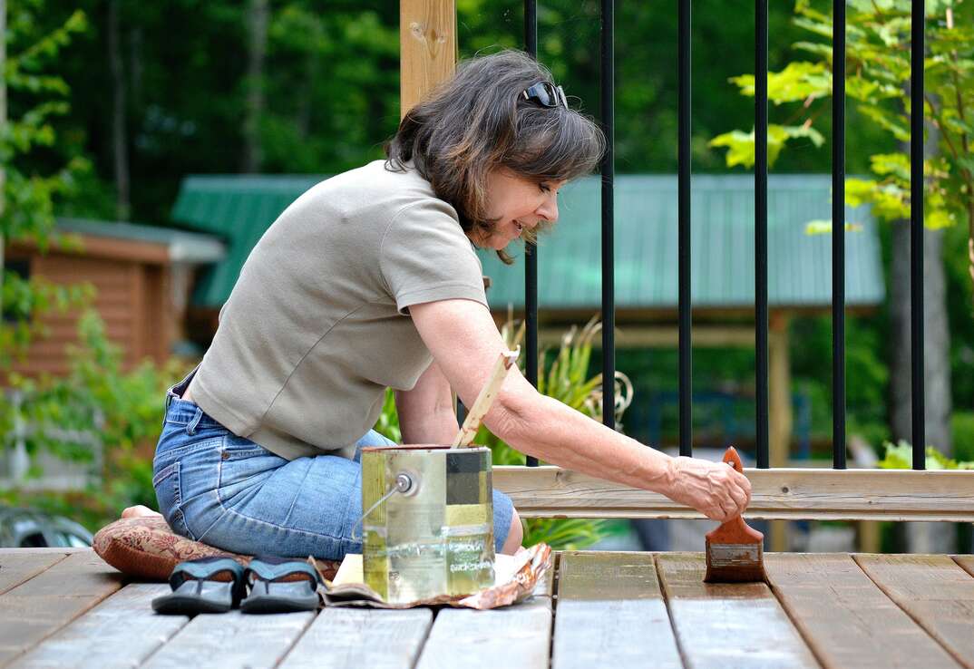 woman applying stain to exterior deck