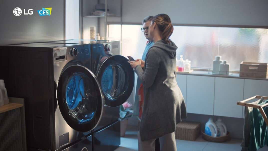 A woman shows another person a newfangled washer and dryer in a home laundry room
