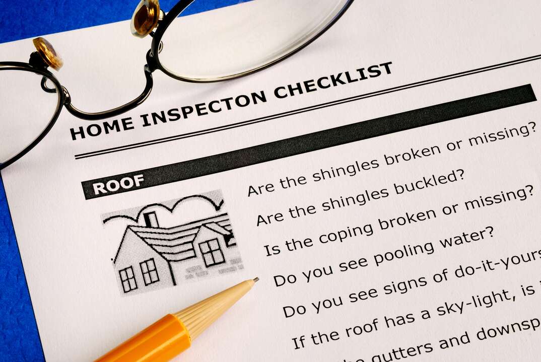 A document labeled Home Inspection Checklist and bearing a small drawing of a house as well as a list of inspection related questions sits on a blue surface with a mechanical pencil and a pair of eyeglasses resting on top of it, document, home inspection checklist, home inspection, inspection checklist, eyeglasses, glasses, pencil, pen, mechanical pencil, blue background