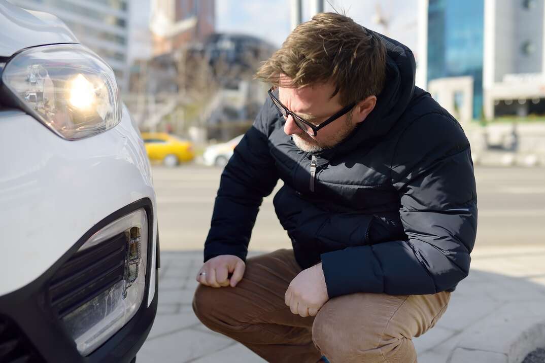 Man is watching broken automobile headlight. Destroyed front light on the left side. Car crash or accident. Insurance, repair. Repair of auto.