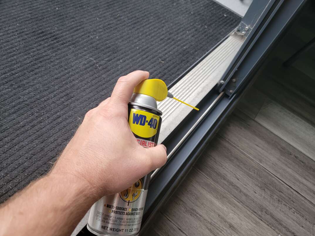 Human hand using WD-40 to lubricate sliding glass door track.