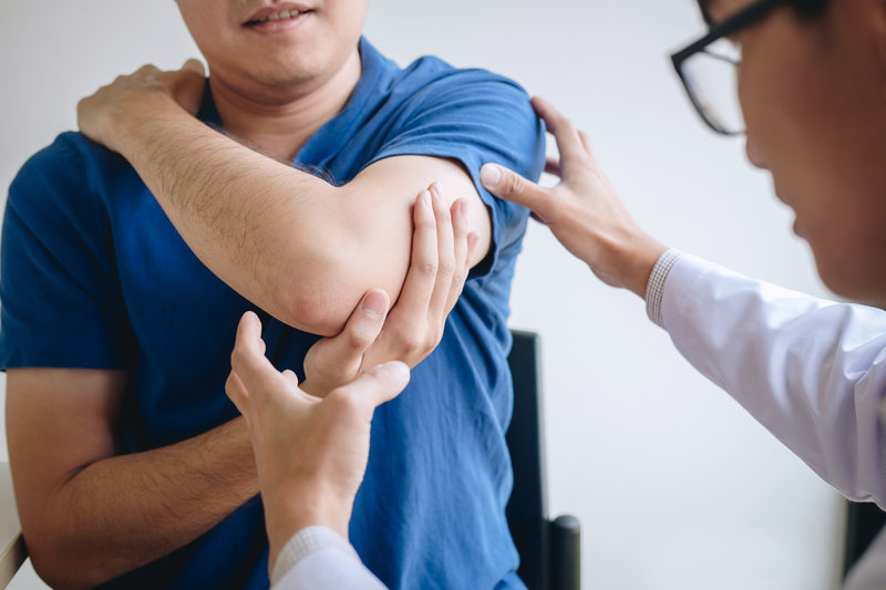 Doctor physiotherapist assisting a male patient while giving exercising treatment massaging the arm of patient in a physio room, rehabilitation physiotherapy concept.